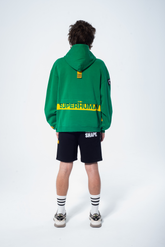 Model in the Haresquare Superhuman Abundant Green hoodie with yellow print, styled with Haresquare black shorts – unisex luxury streetwear from Ireland.